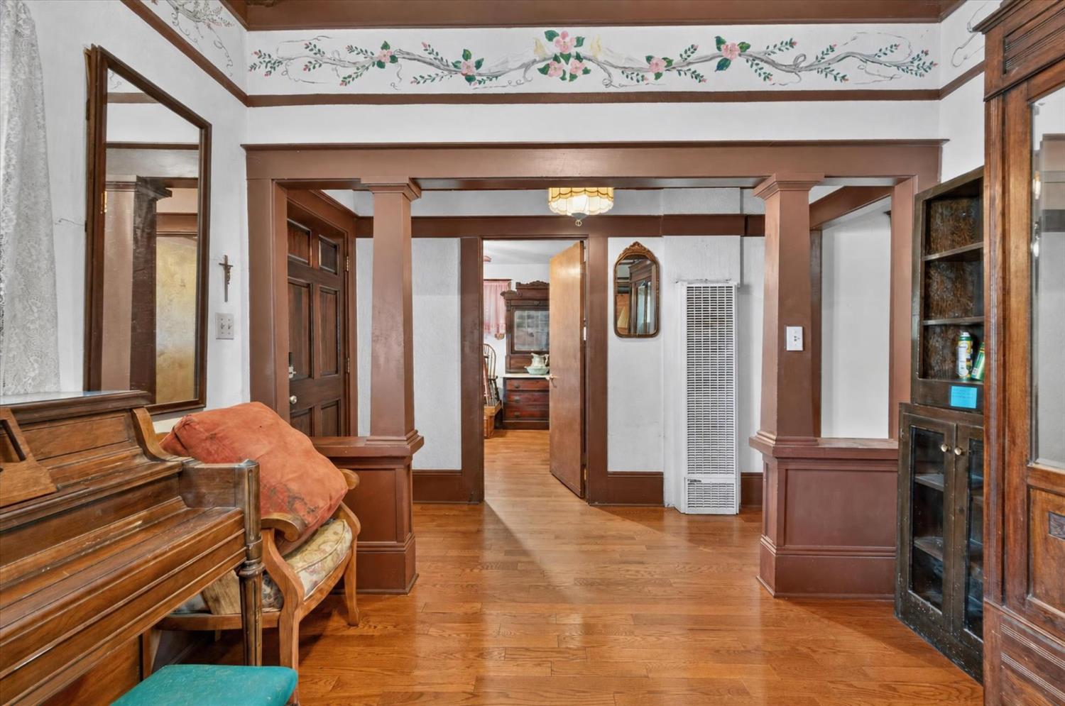 Furnished room with hardwood floors, dark wood columns, a piano, and floral wall trim.