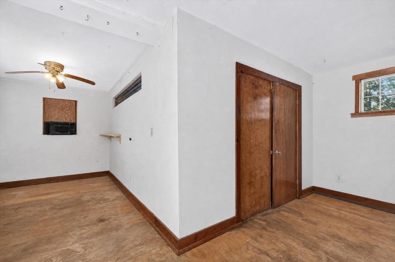 Empty room with worn wood flooring, a ceiling fan, and dark wood closet doors.