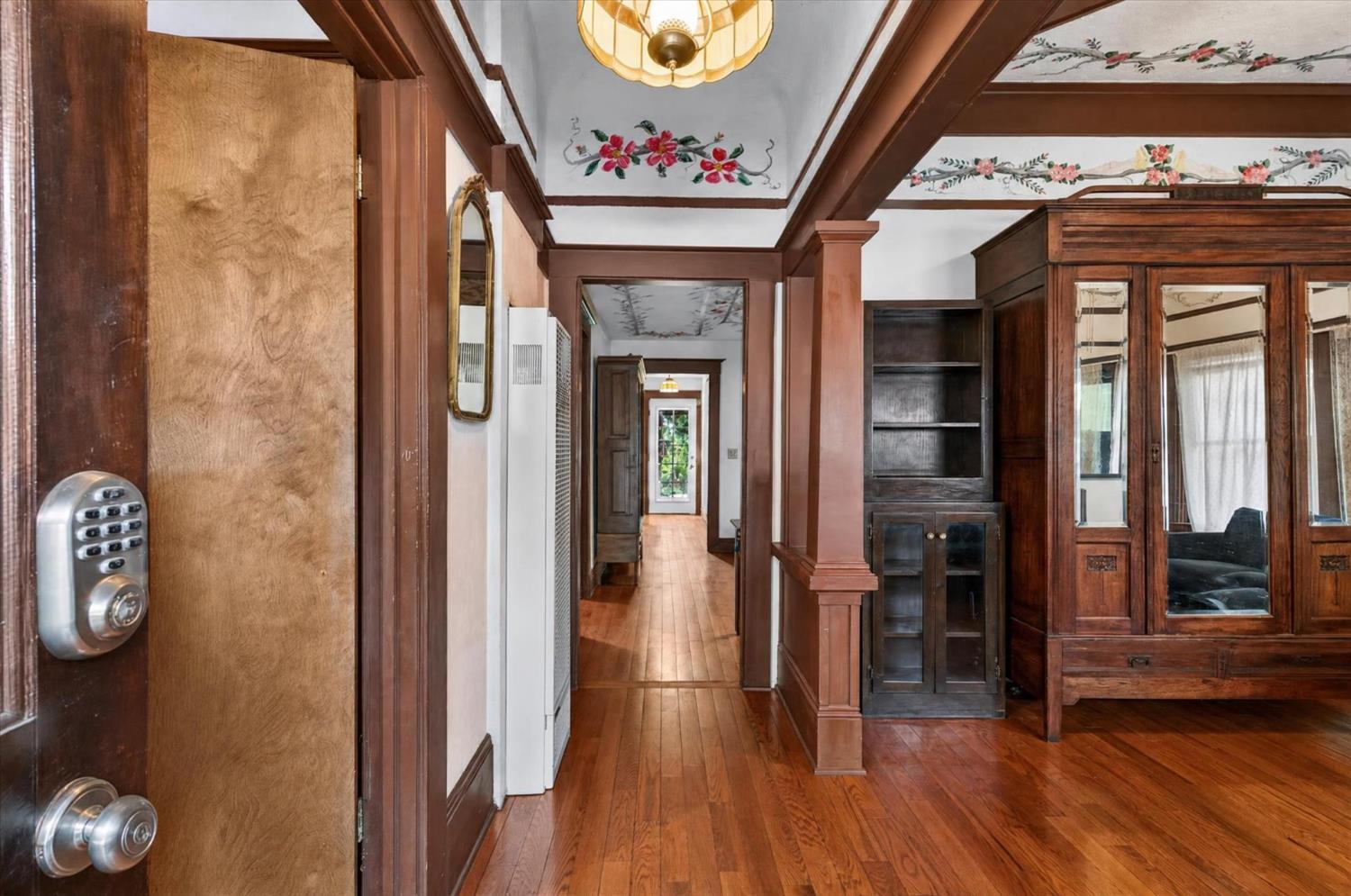 Wood-paneled hallway with floral ceiling details, built-in cabinetry, and a view toward greenery.