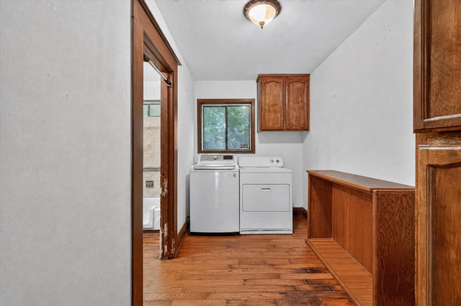 Laundry room with washer and dryer, wood cabinetry, and hardwood floors.