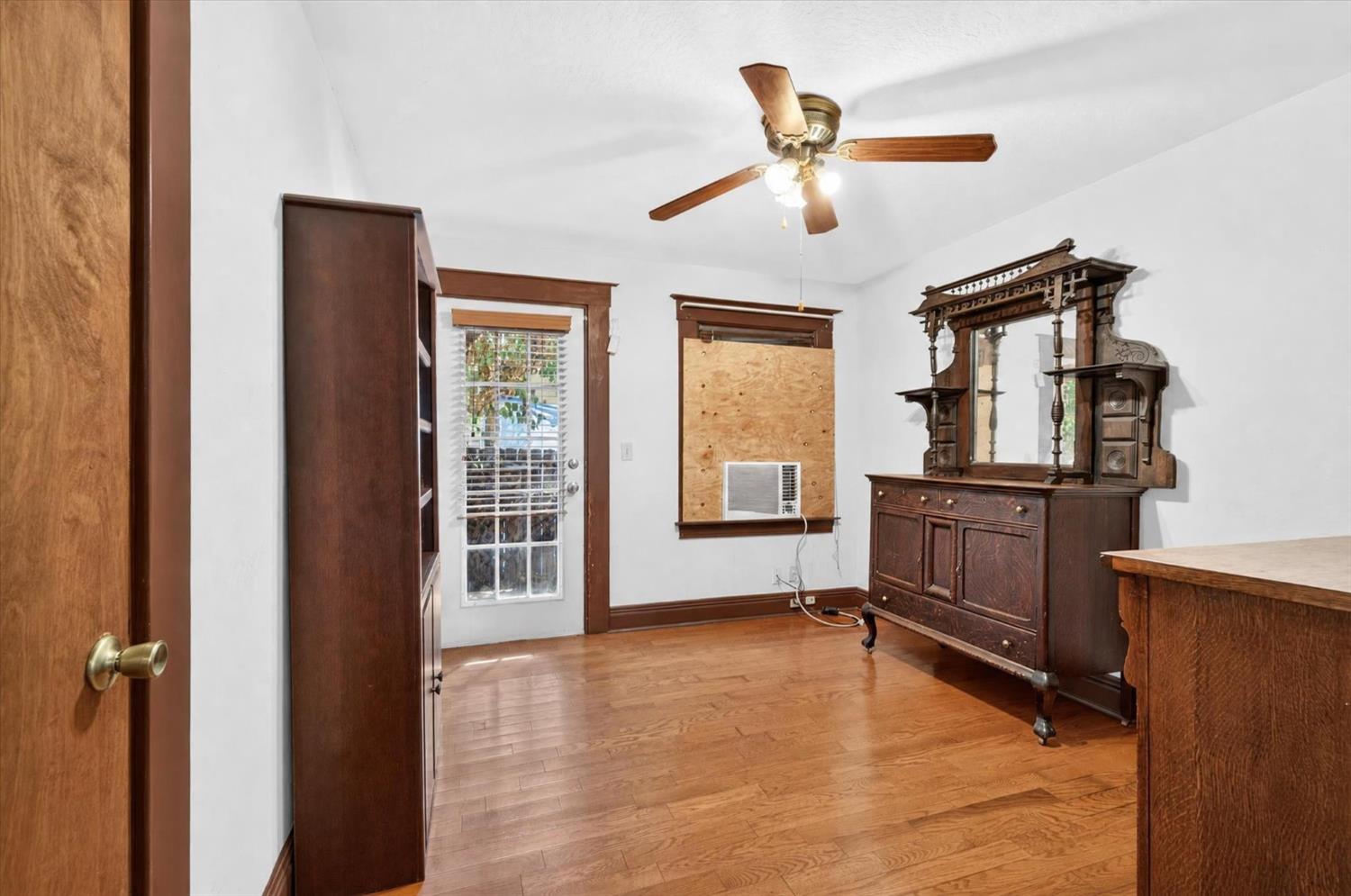 Room with hardwood floors, ornate dark wood dresser and mirror, ceiling fan, and window air conditioner.