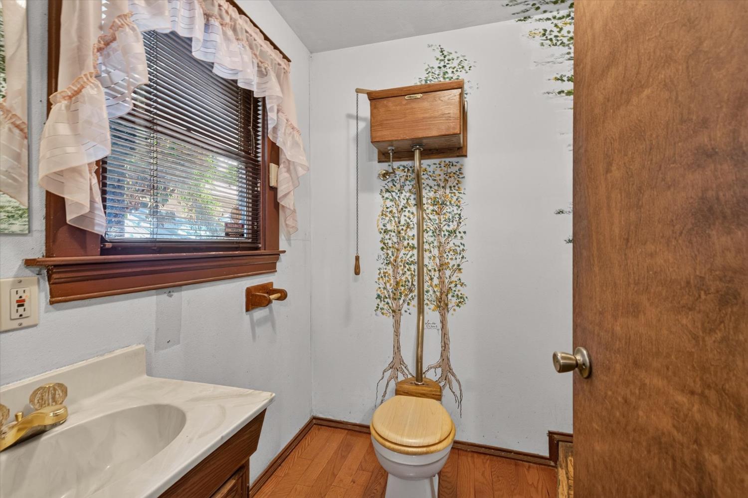 Bathroom with a tree mural behind the toilet and a wood-finished sink vanity.