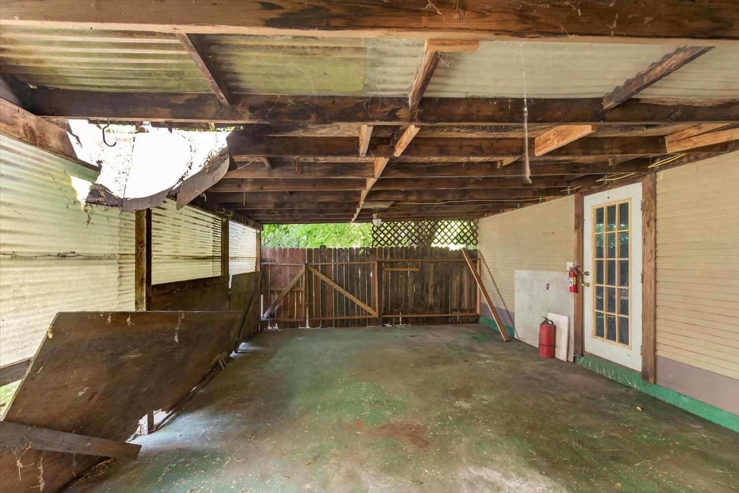 Covered outdoor area with exposed wood beams, concrete floor, and a wooden gate.