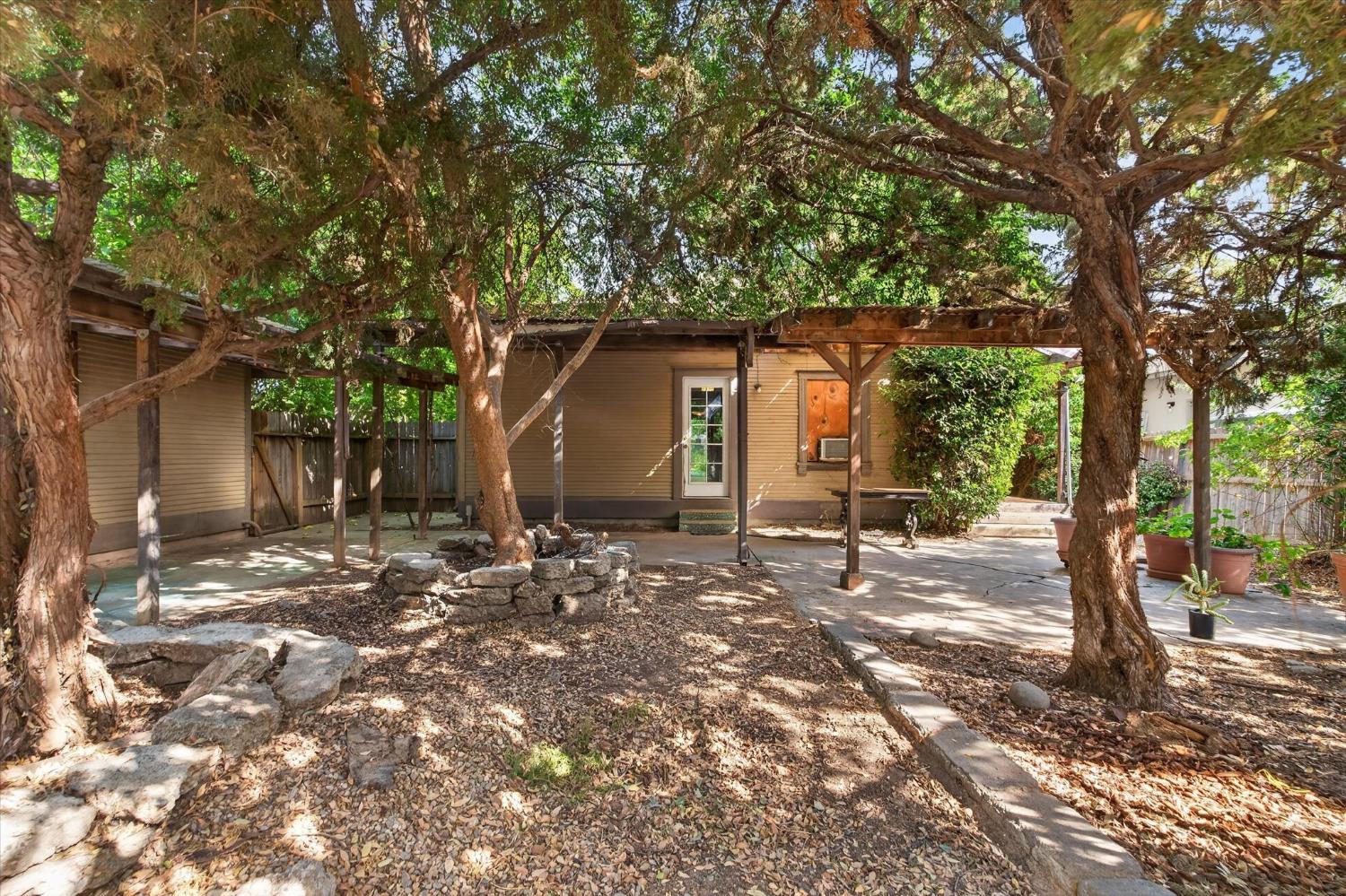 Home’s shaded backyard with a covered patio beneath large mature trees.