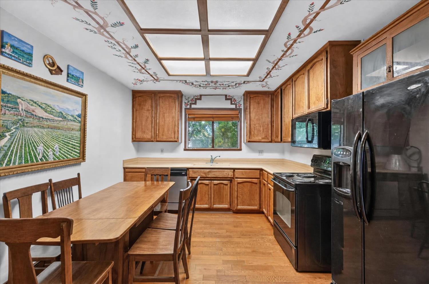 Kitchen with wood cabinets, black appliances, a dining table, and a painted floral ceiling.