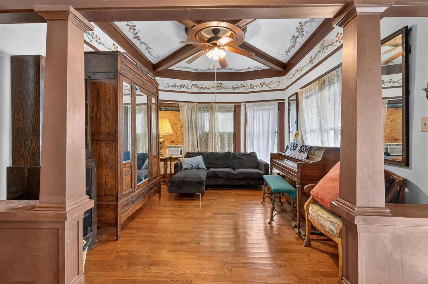 Living room with an ornate painted ceiling, hardwood floors, sectional sofa, and upright piano.