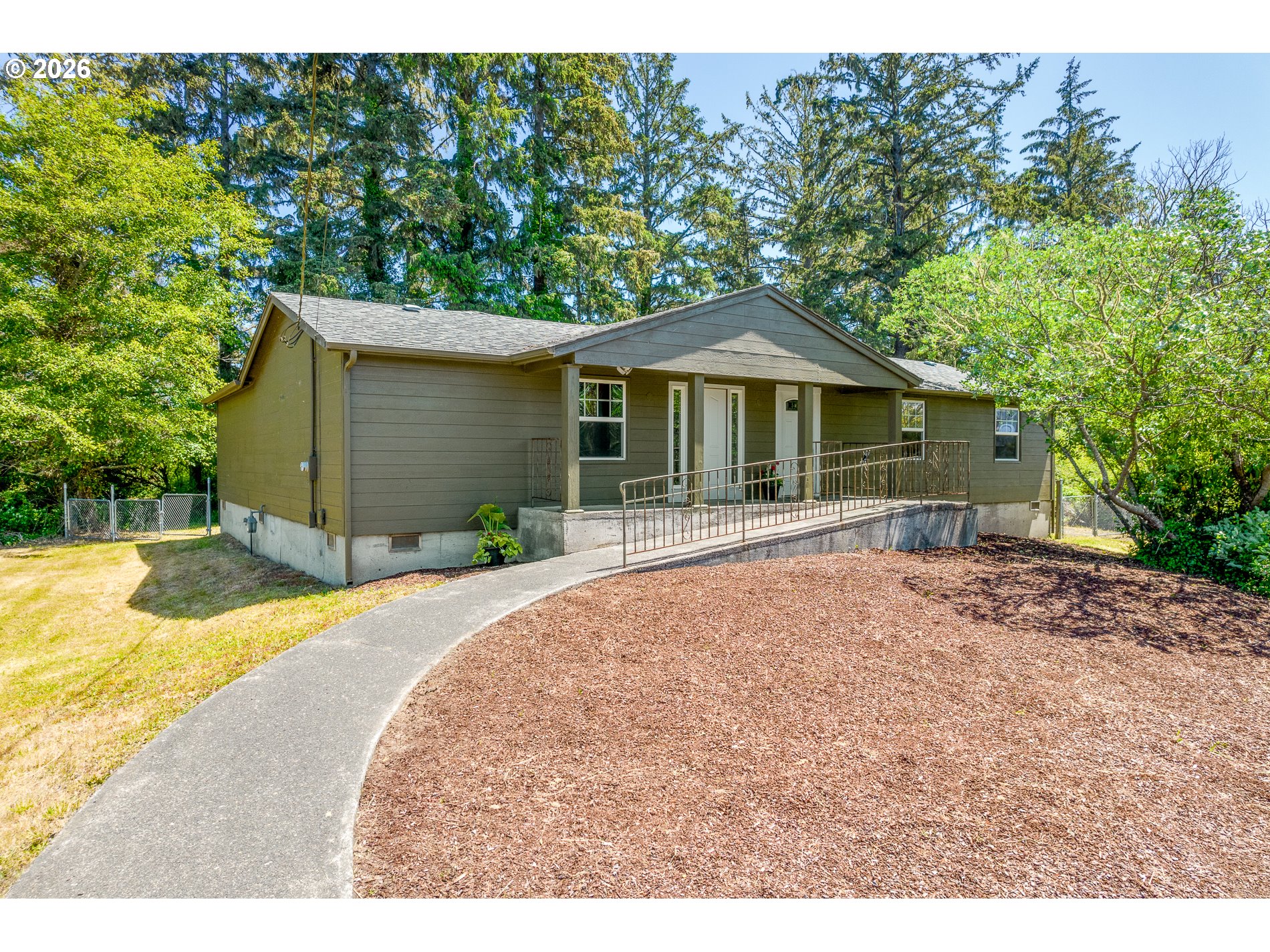 Single-story home with a long ramp and railing, surrounded by mature trees.