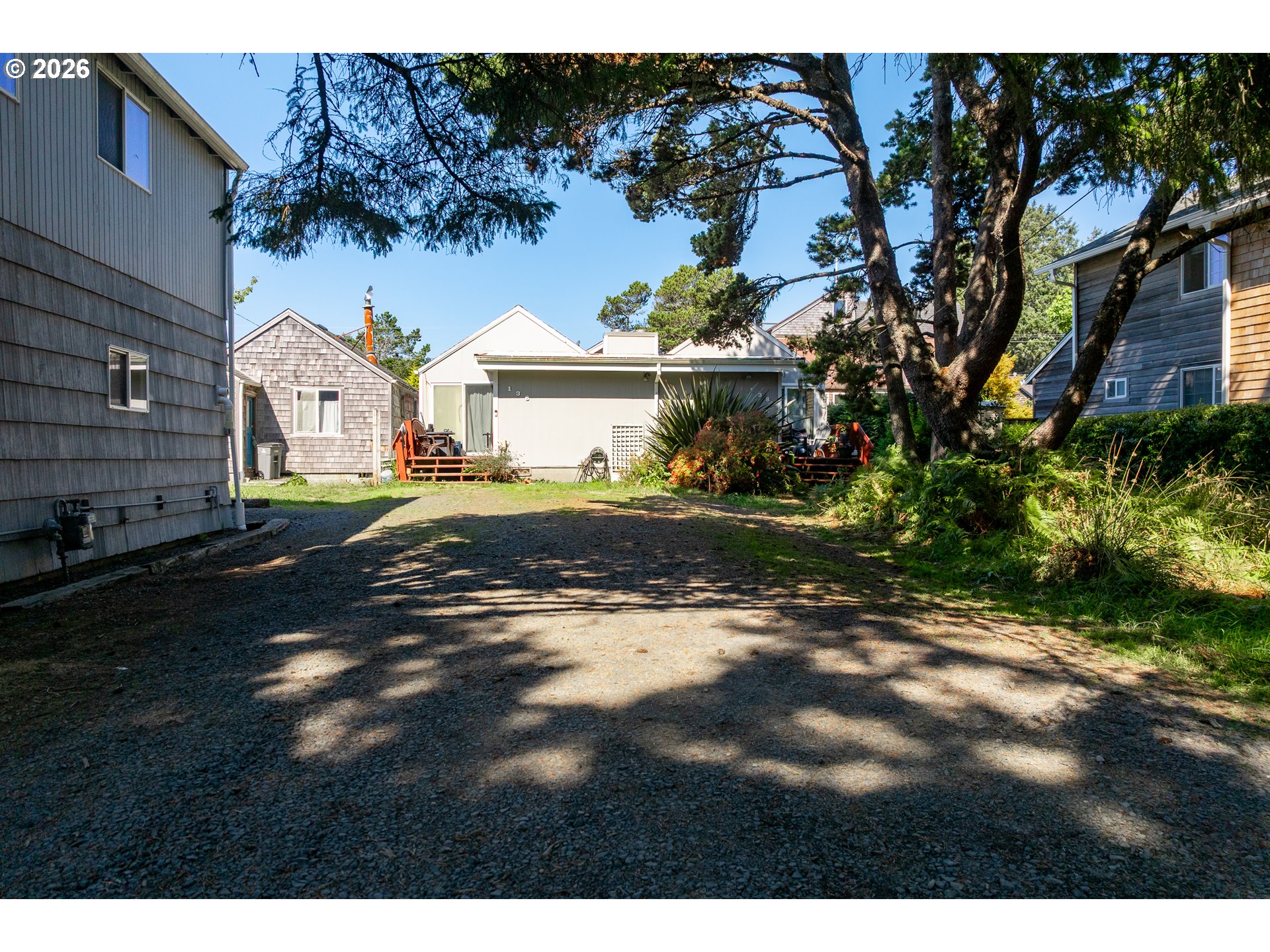 Gravel courtyard between coastal homes, shaded by mature trees.