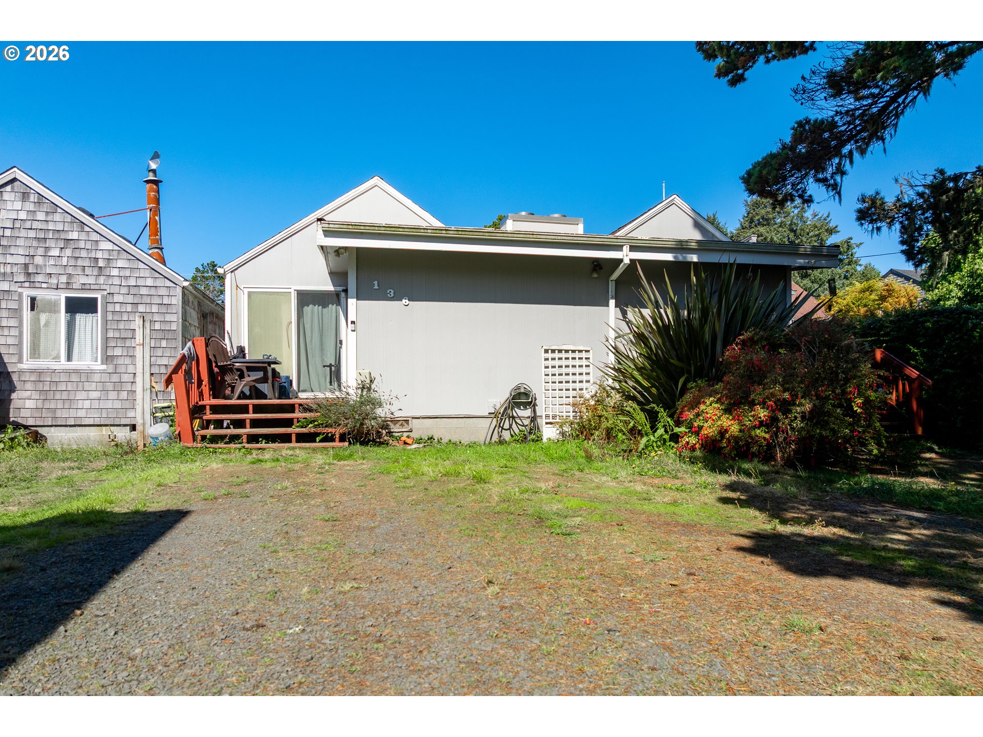 Light gray home with a red deck, patio chairs, and a gravel yard.