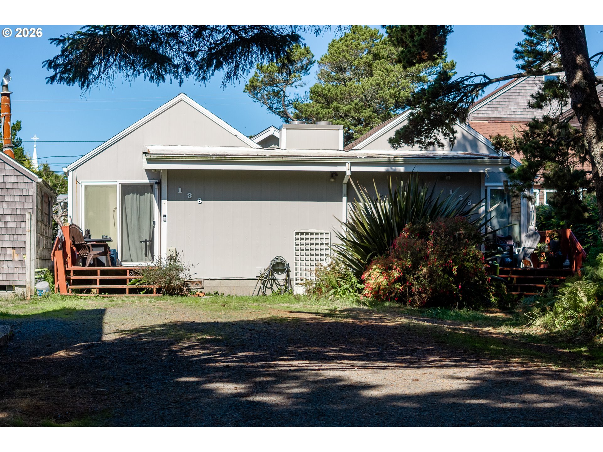 Light-colored home with a covered porch, wooden steps, patio chairs, and mature landscaping.