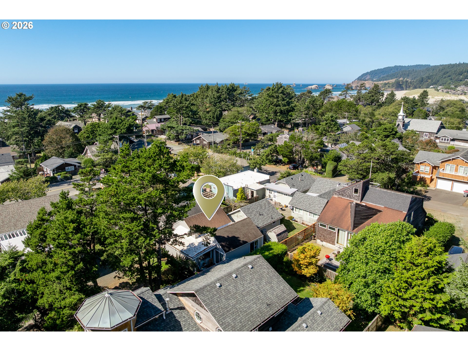 Aerial view of a Cannon Beach neighborhood and Pacific coast, with the property marked by a pin.