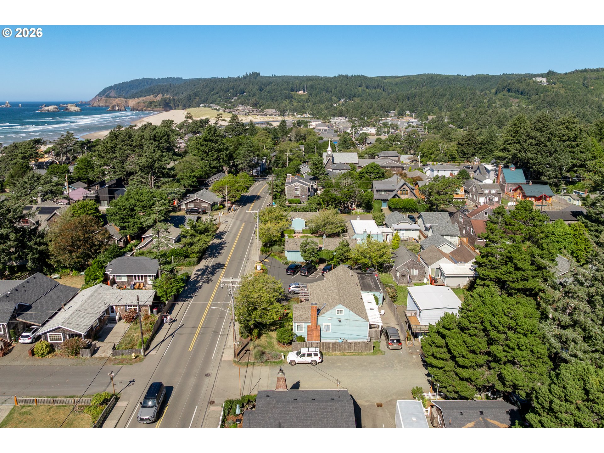 Aerial view of Cannon Beach homes, sandy shoreline, ocean, and forested hills.