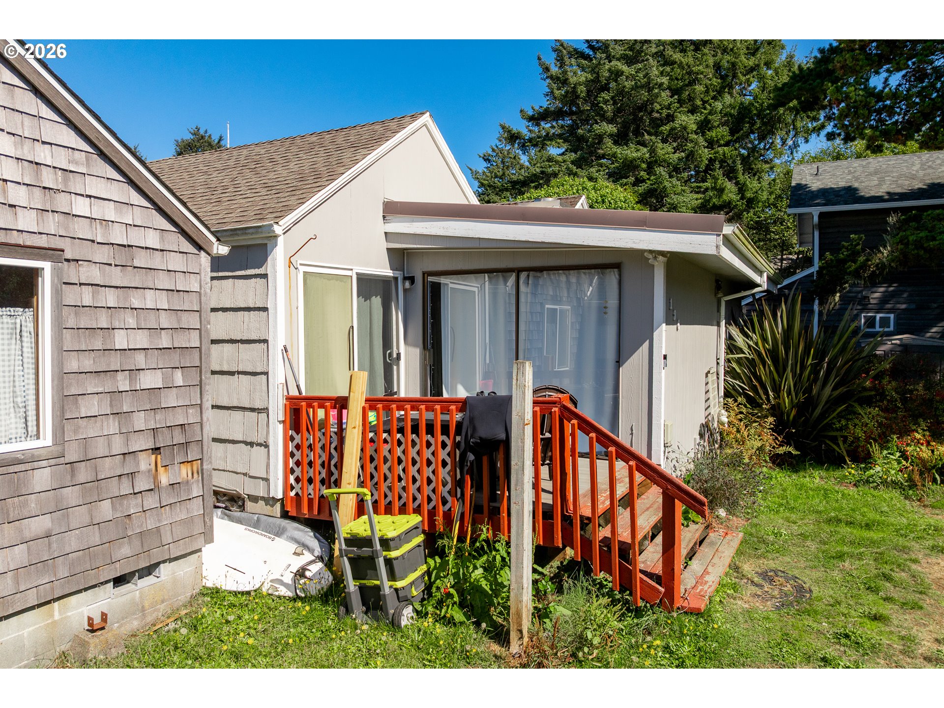 House exterior with a red-railed deck, sliding glass doors, and a grassy yard.