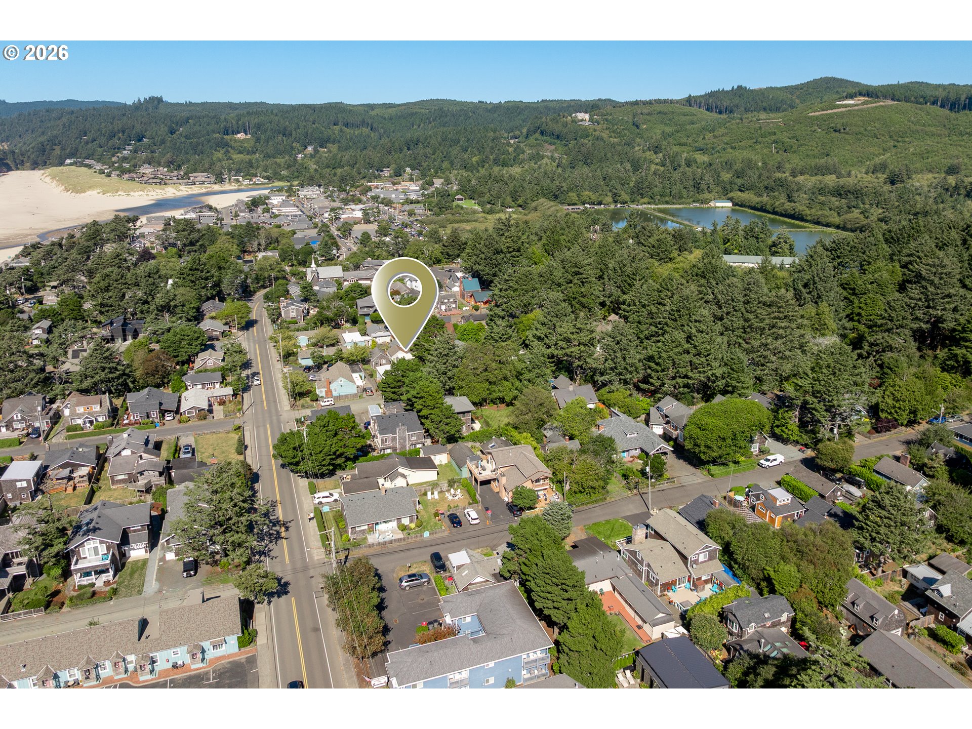 Aerial view of the neighborhood, with a pin marking the property near the beach and forested hills.