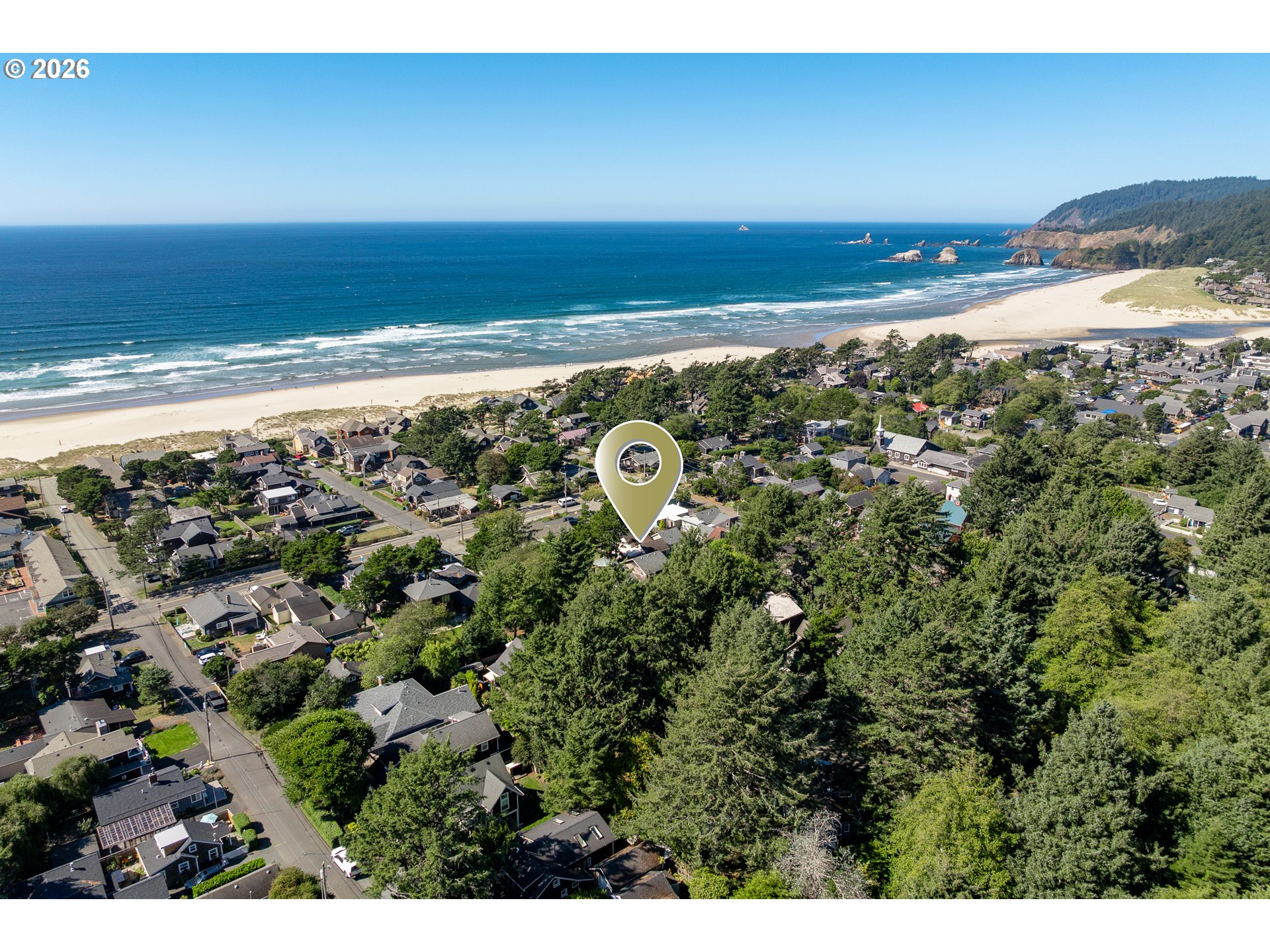 Aerial view of a Cannon Beach neighborhood beside a sandy beach, ocean, and forested headland.