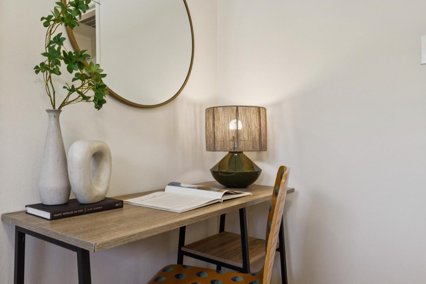 Home workspace with a wood desk, lit lamp, open books, and round mirror.