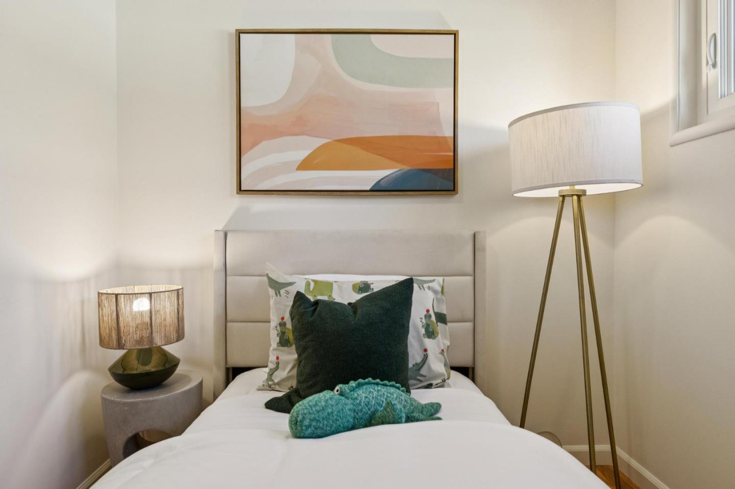 Bedroom with a single bed, patterned pillows, framed abstract art, and bedside lamps.