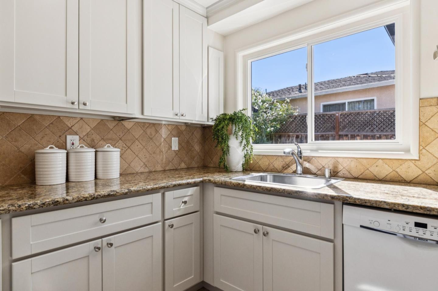 Bright kitchen with white cabinets, granite counters, and a sink beneath a large window.