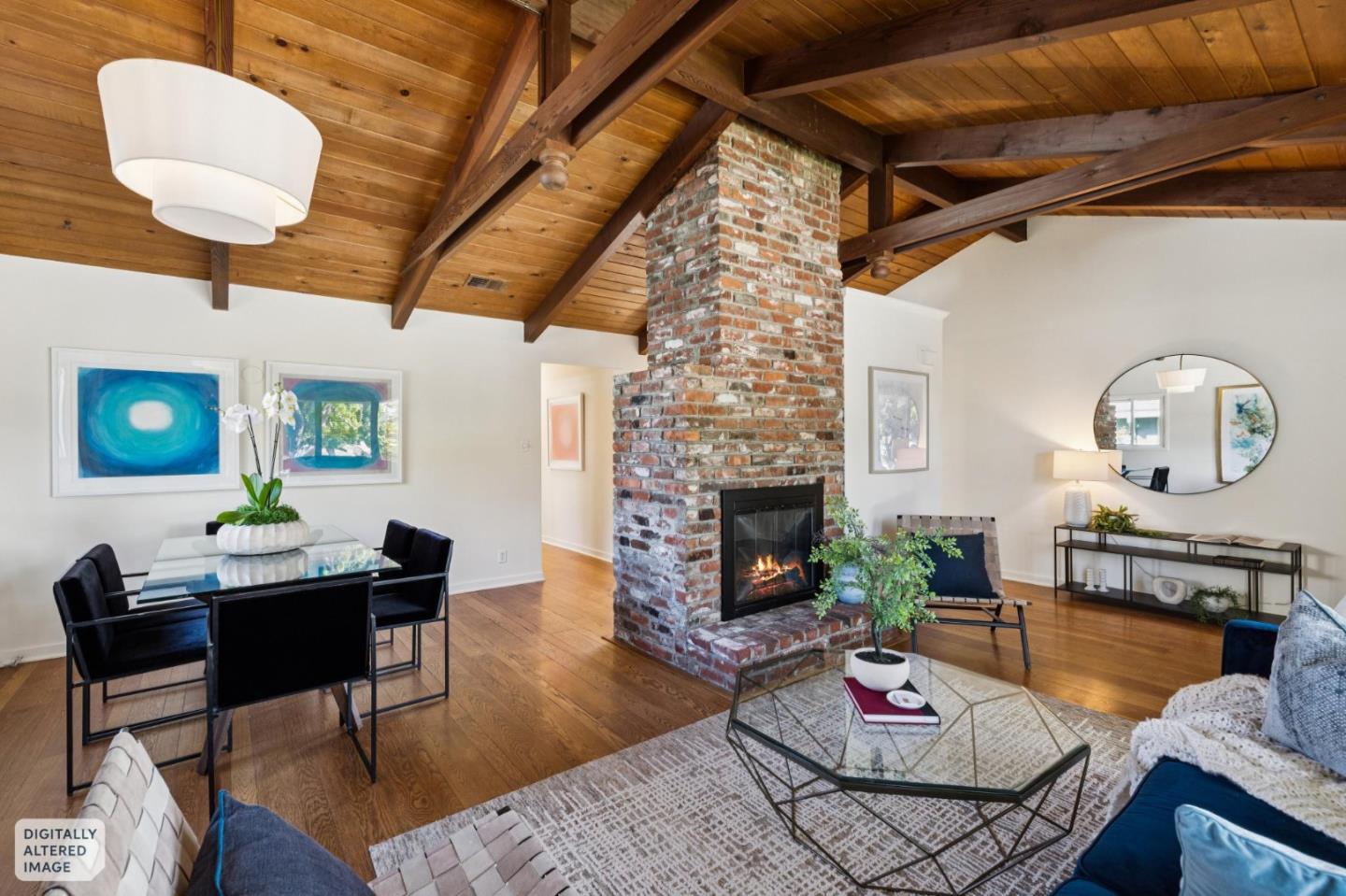 Living and dining room with a vaulted wood ceiling, exposed beams, and central brick fireplace.