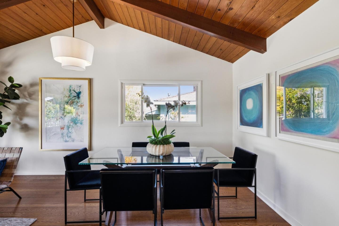 Dining room with a glass table, black chairs, and a vaulted wood-plank ceiling.
