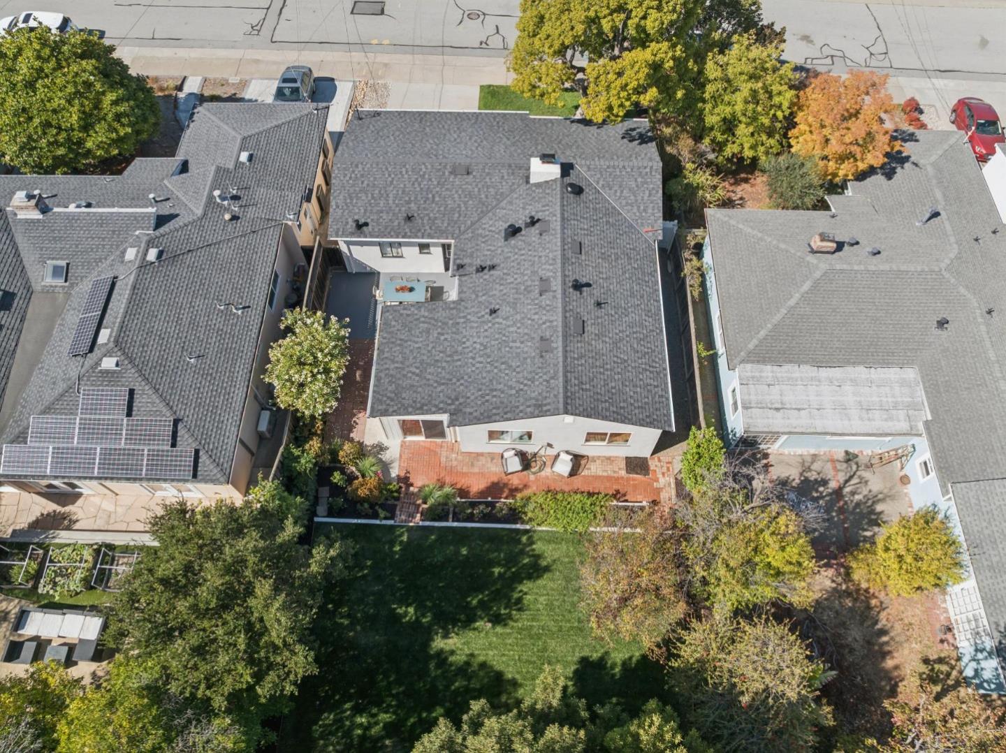 Aerial view of a San Mateo home with a brick patio, green backyard, and autumn trees.