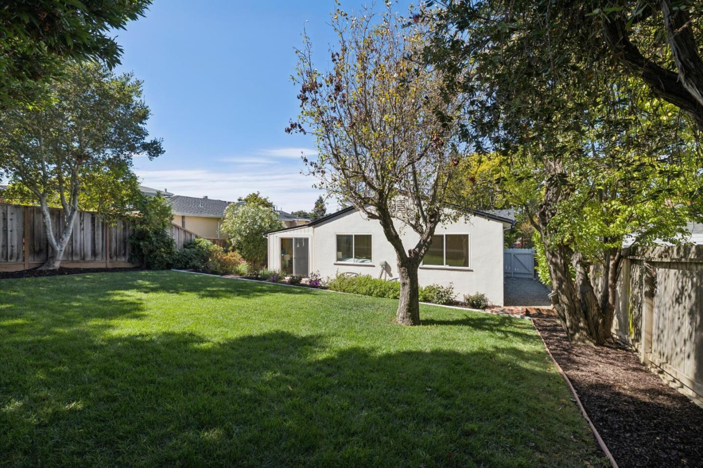 Fenced backyard with a broad lawn, mature trees, and the rear of a single-story home.