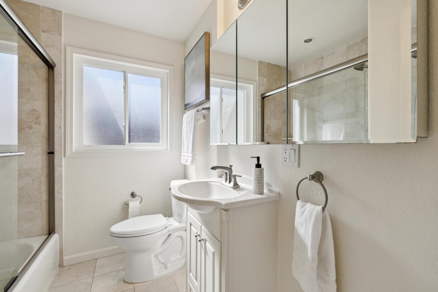 Bright bathroom with a white vanity, mirrored cabinets, and a glass-enclosed tiled shower.