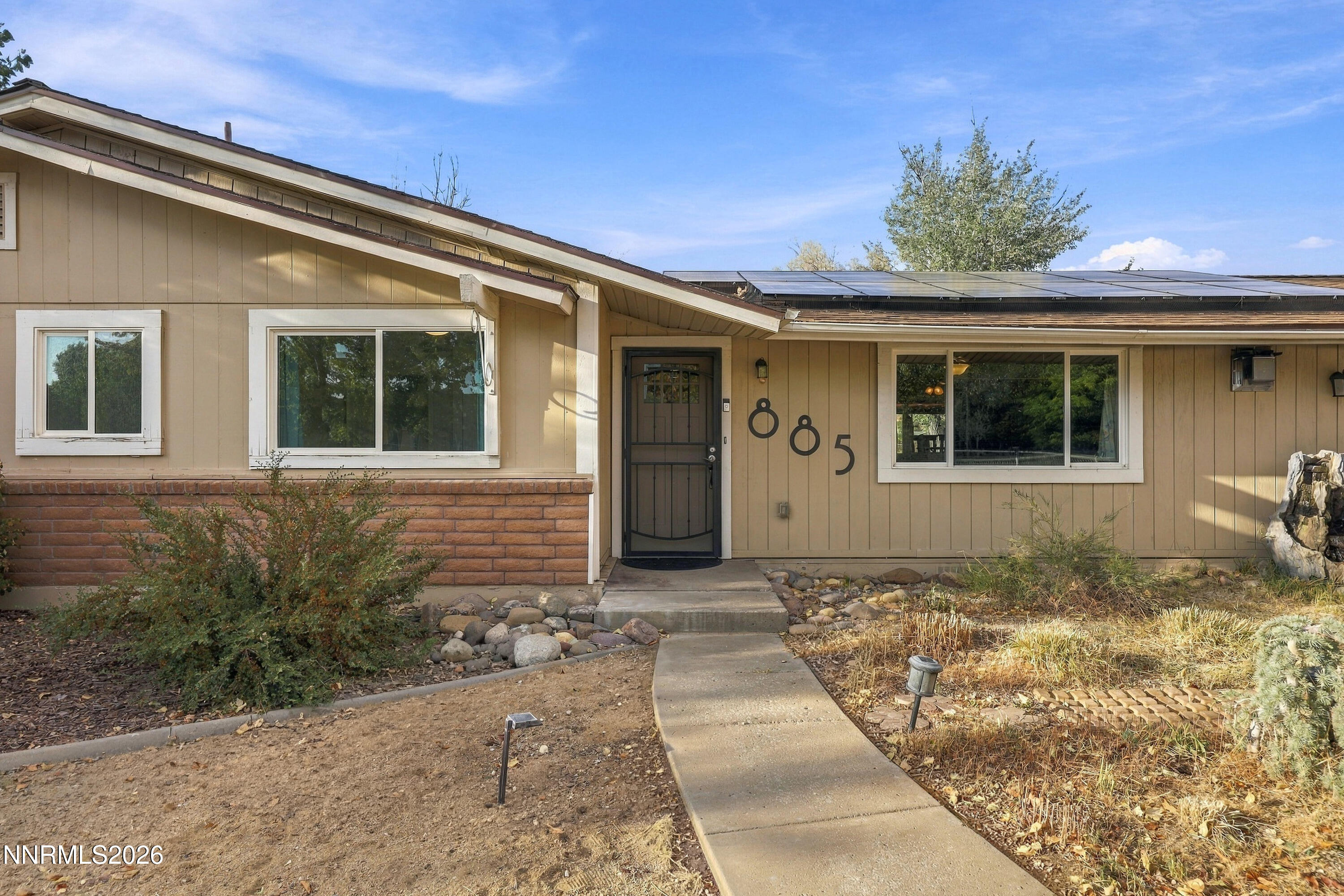 Single-story tan home with solar panels, brick lower facade, and a walkway leading to the front door.