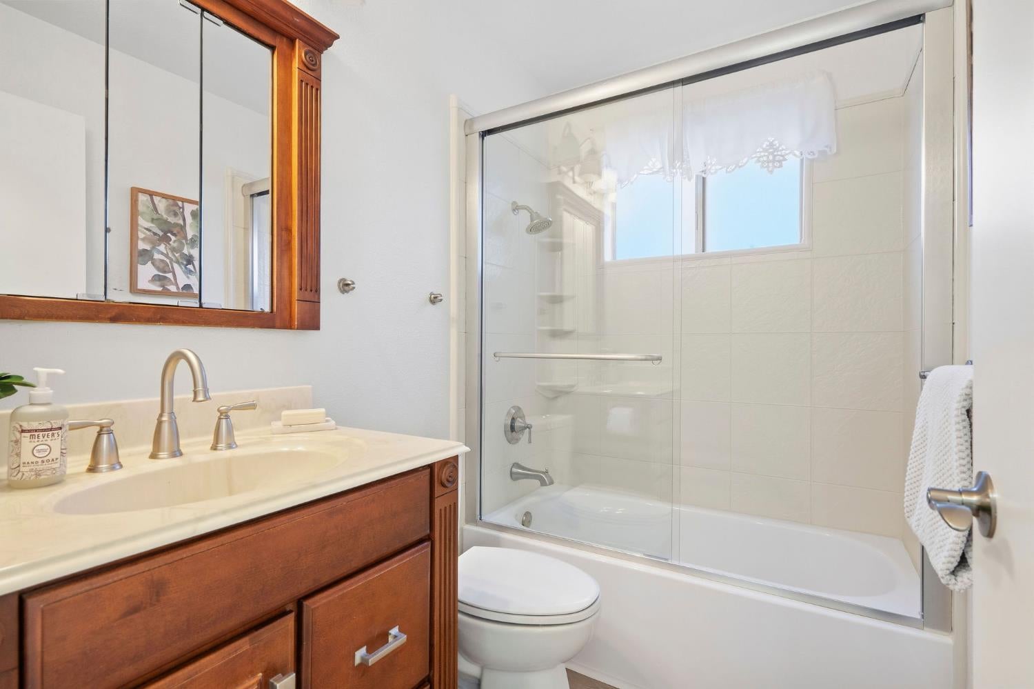 Bathroom with a wood vanity and mirrored cabinet beside a glass-enclosed tub and shower.