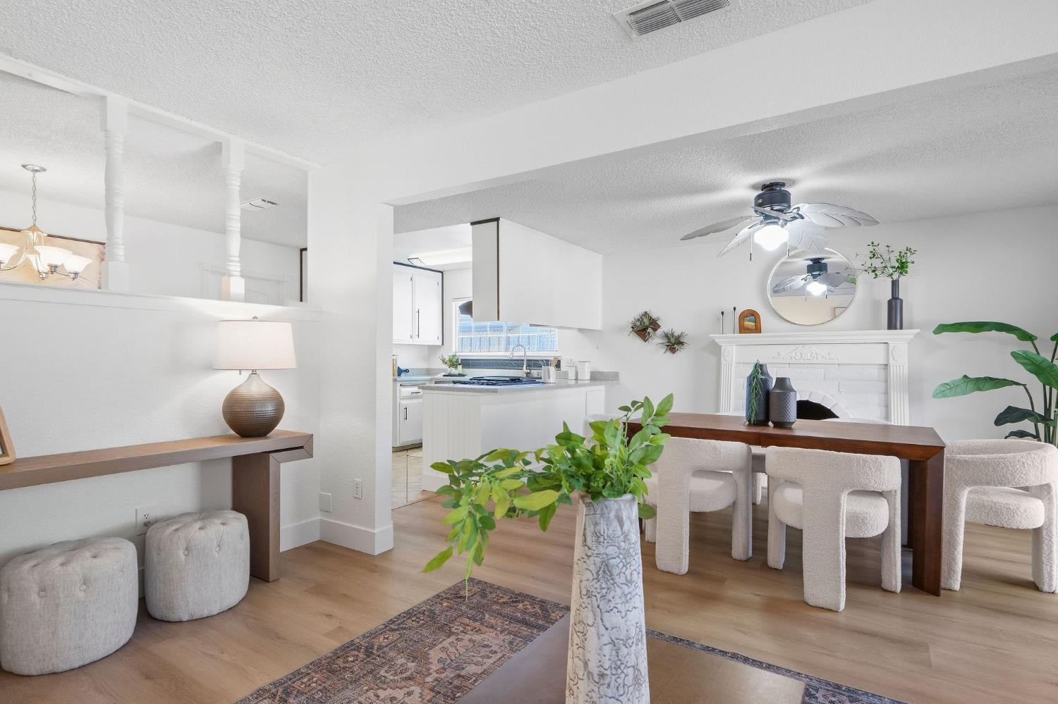 Open-plan dining and living area with kitchen, white fireplace, and dark wood dining table.