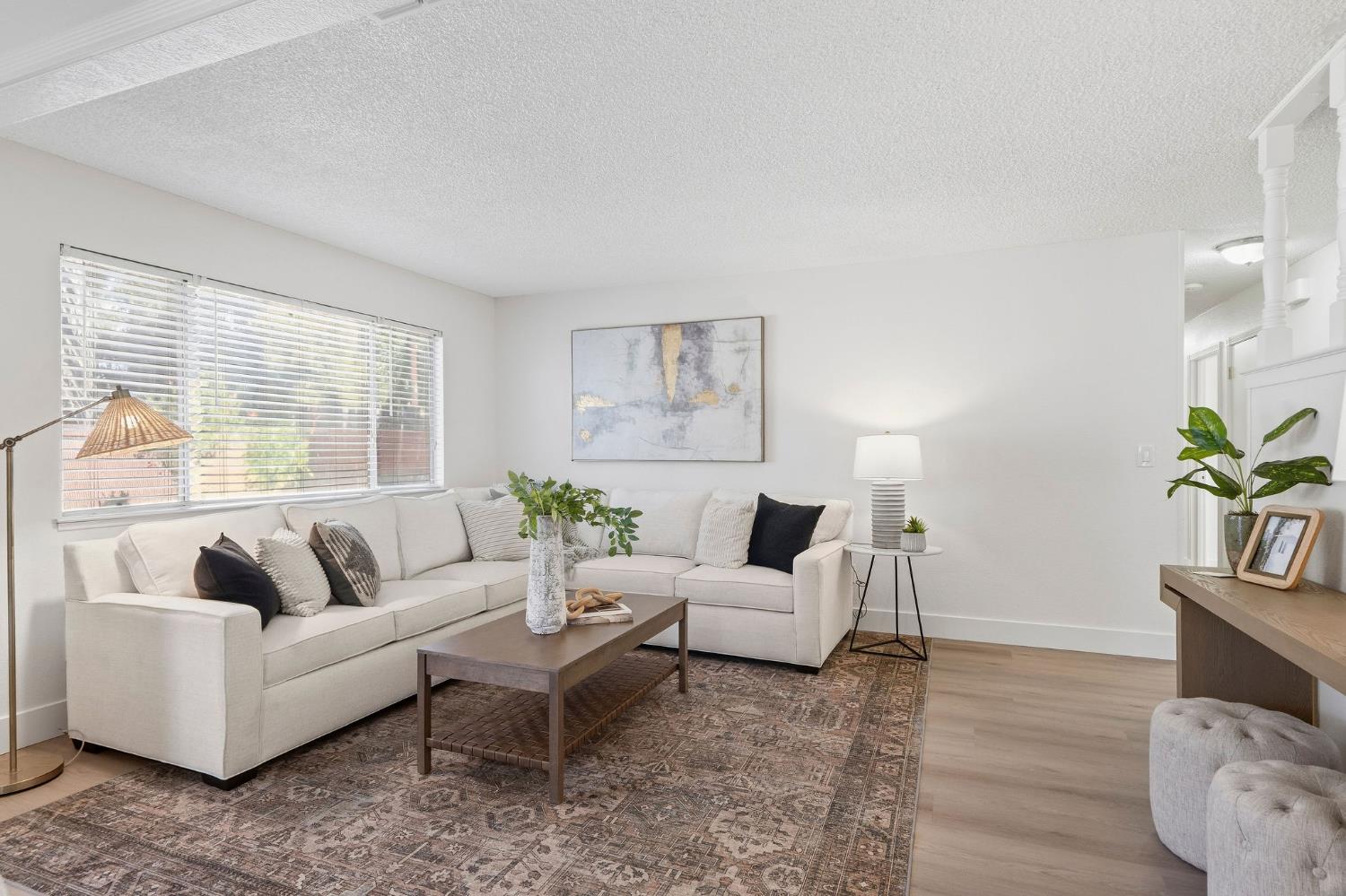 Staged living room with a white sectional, patterned rug, and large window with blinds.