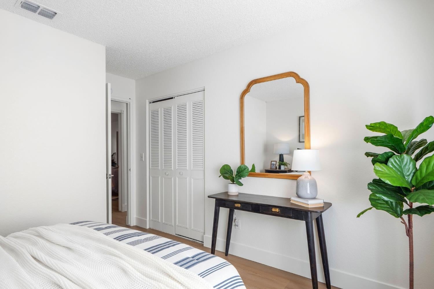 Bedroom with striped bedding, louvered closet doors, and a console table beneath a wood-framed mirror.