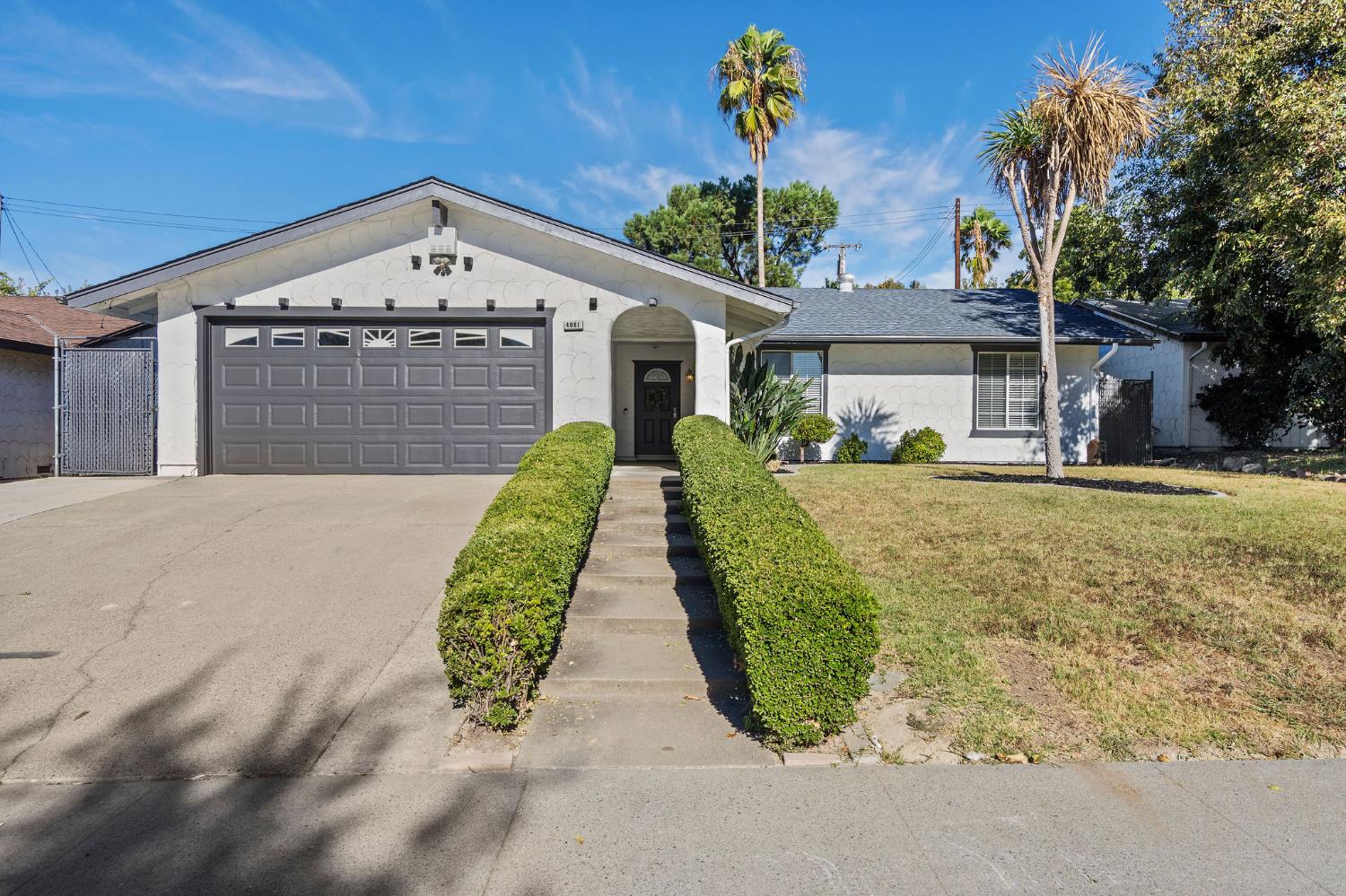 Single-story home with a gray double garage and a hedge-lined front walkway.
