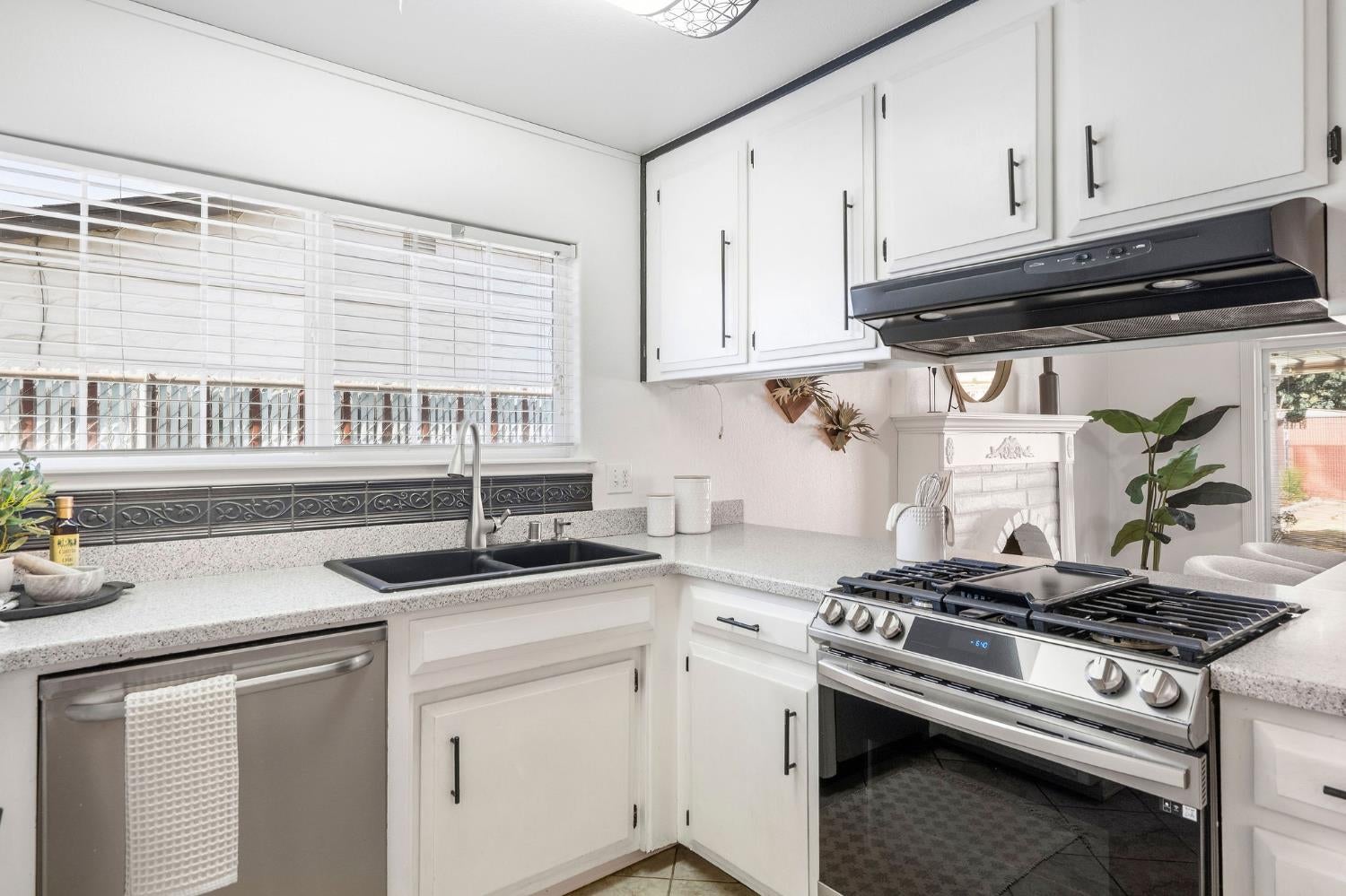 White kitchen with a double sink, stainless appliances, and a decorative fireplace nearby.