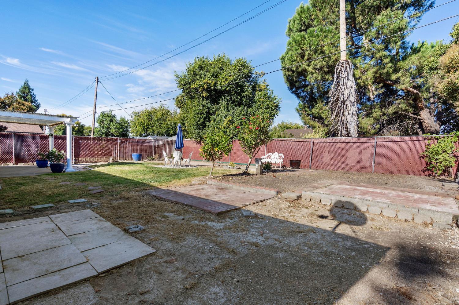 Backyard with paved patio, lawn, outdoor seating, and red privacy fencing.