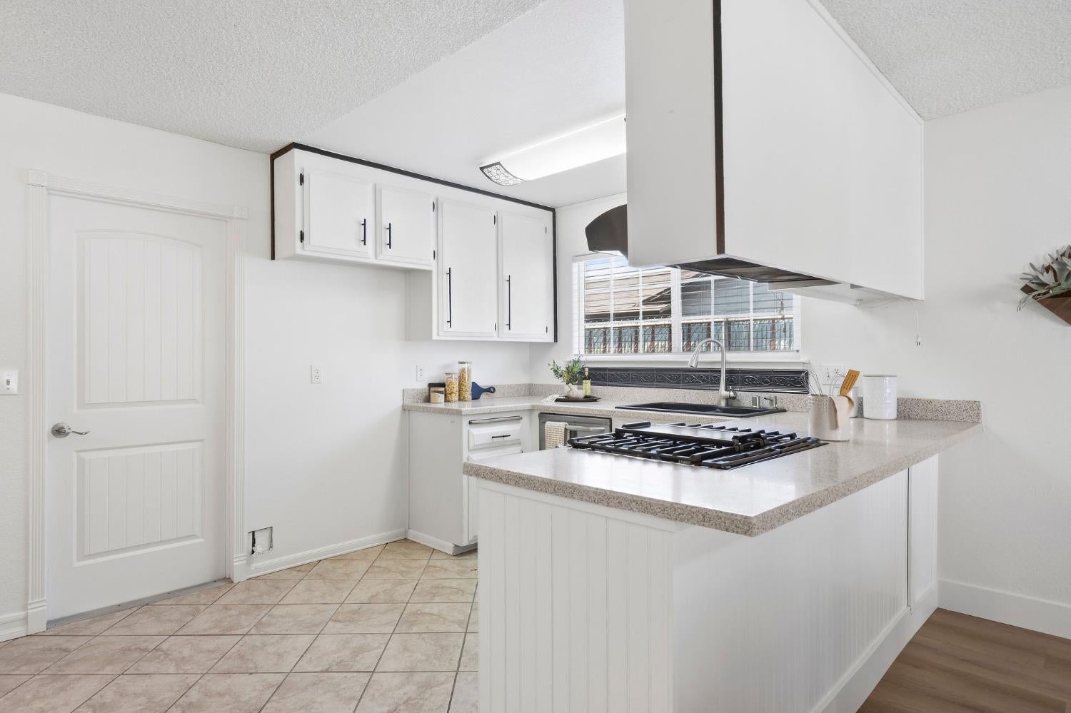 White kitchen with a gas cooktop on the peninsula and a sink beneath the window.