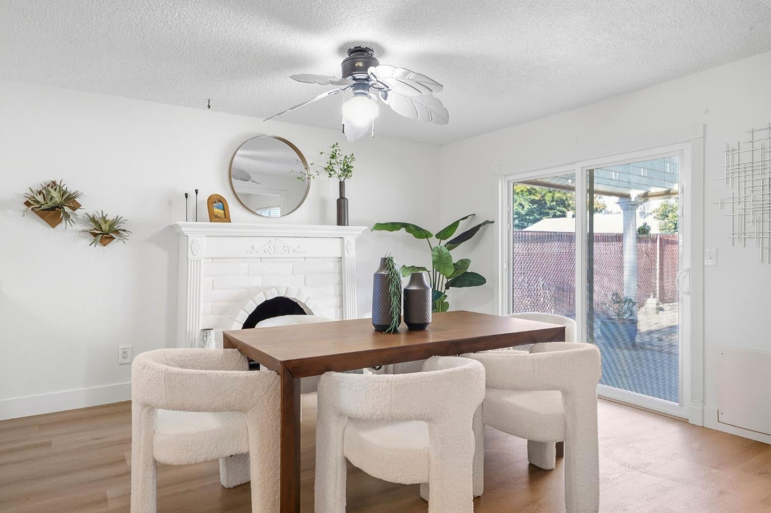 Dining room with a wood table, cream chairs, white fireplace, and sliding glass doors.