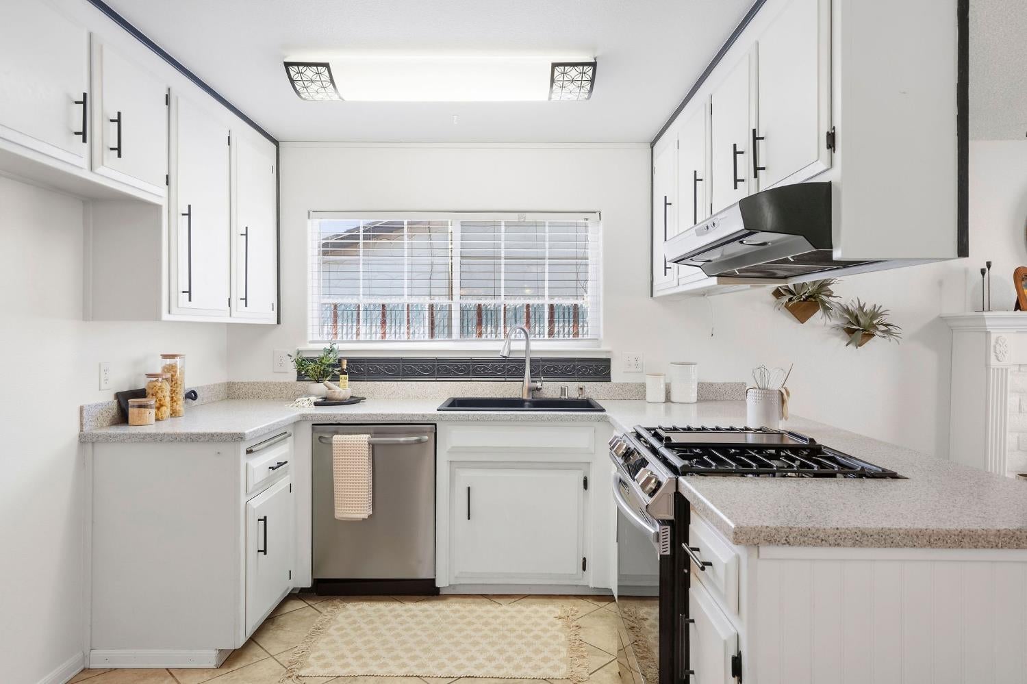 Kitchen with white cabinetry, a gas range, and a sink beneath a window with blinds.