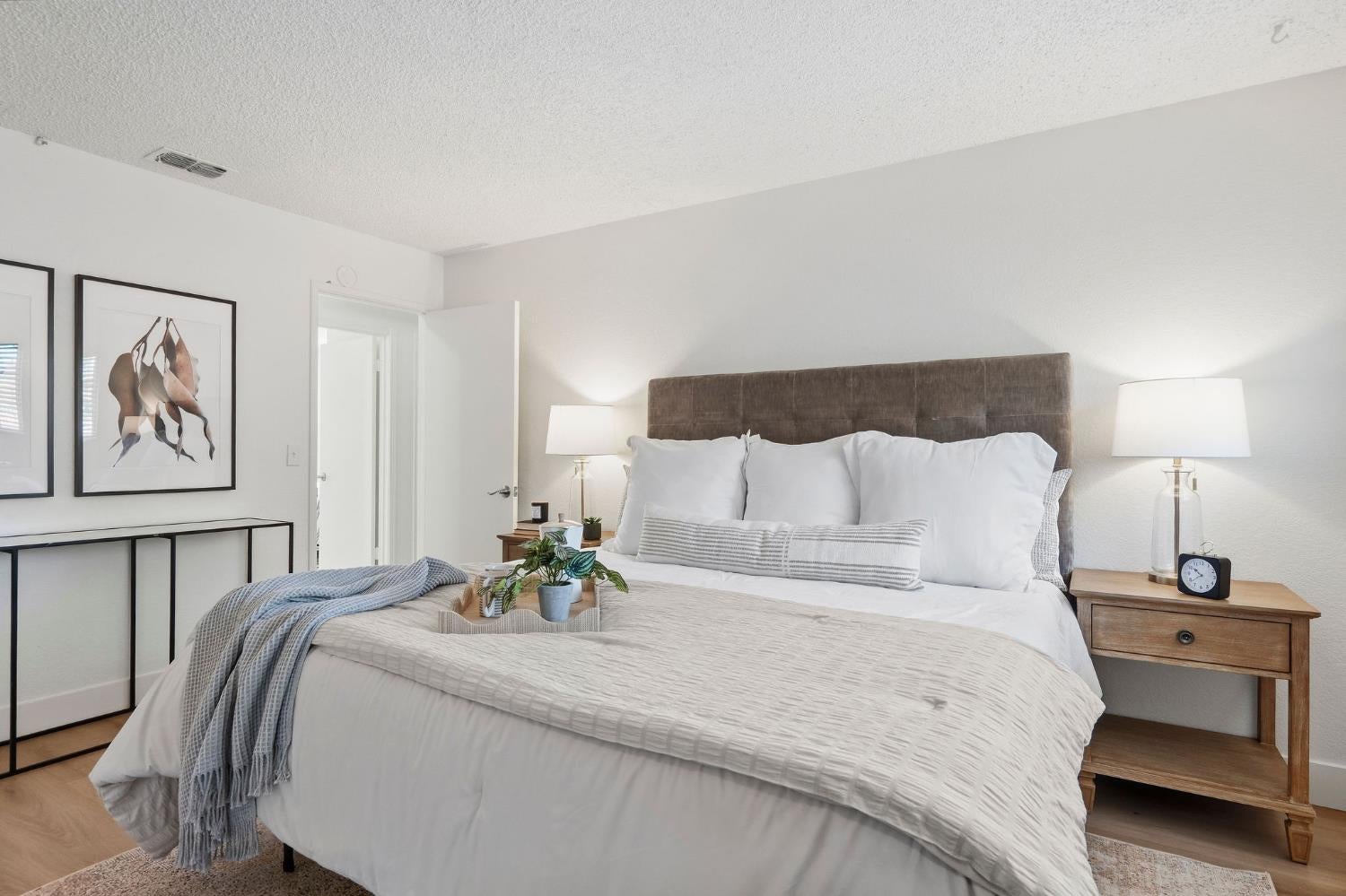 Staged bedroom with white bedding, a tall brown upholstered headboard, and matching bedside lamps.