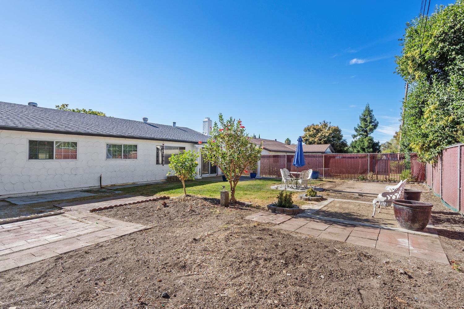 Backyard with paved patio paths, outdoor seating, mature trees, and a red fence.