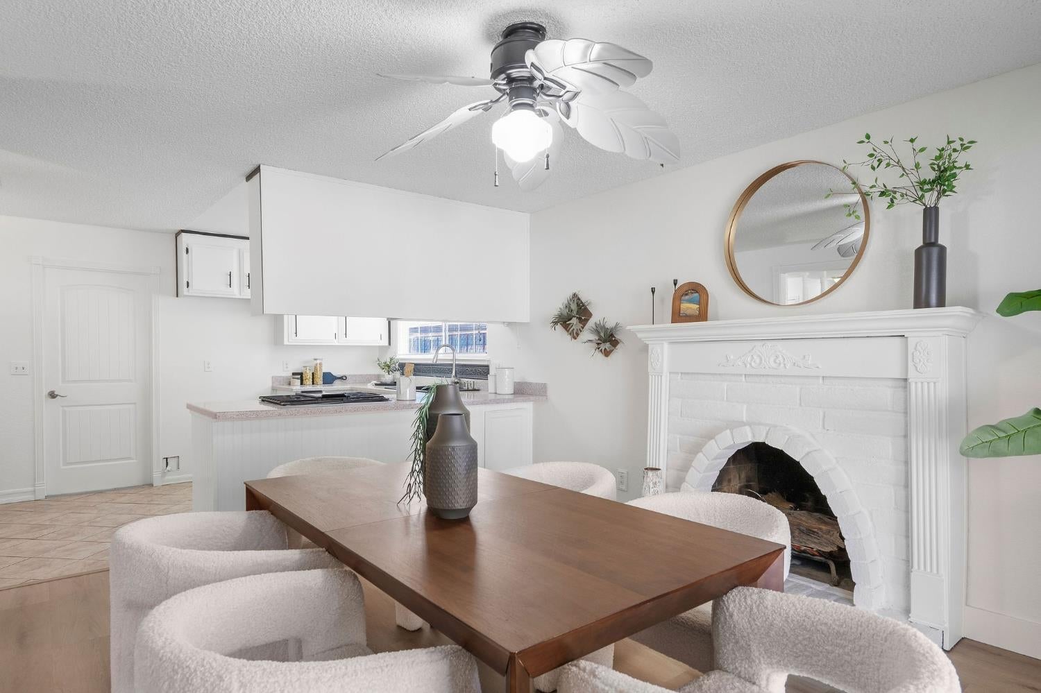 Dining area with a dark wood table, upholstered chairs, and ornate white fireplace beside the kitchen.