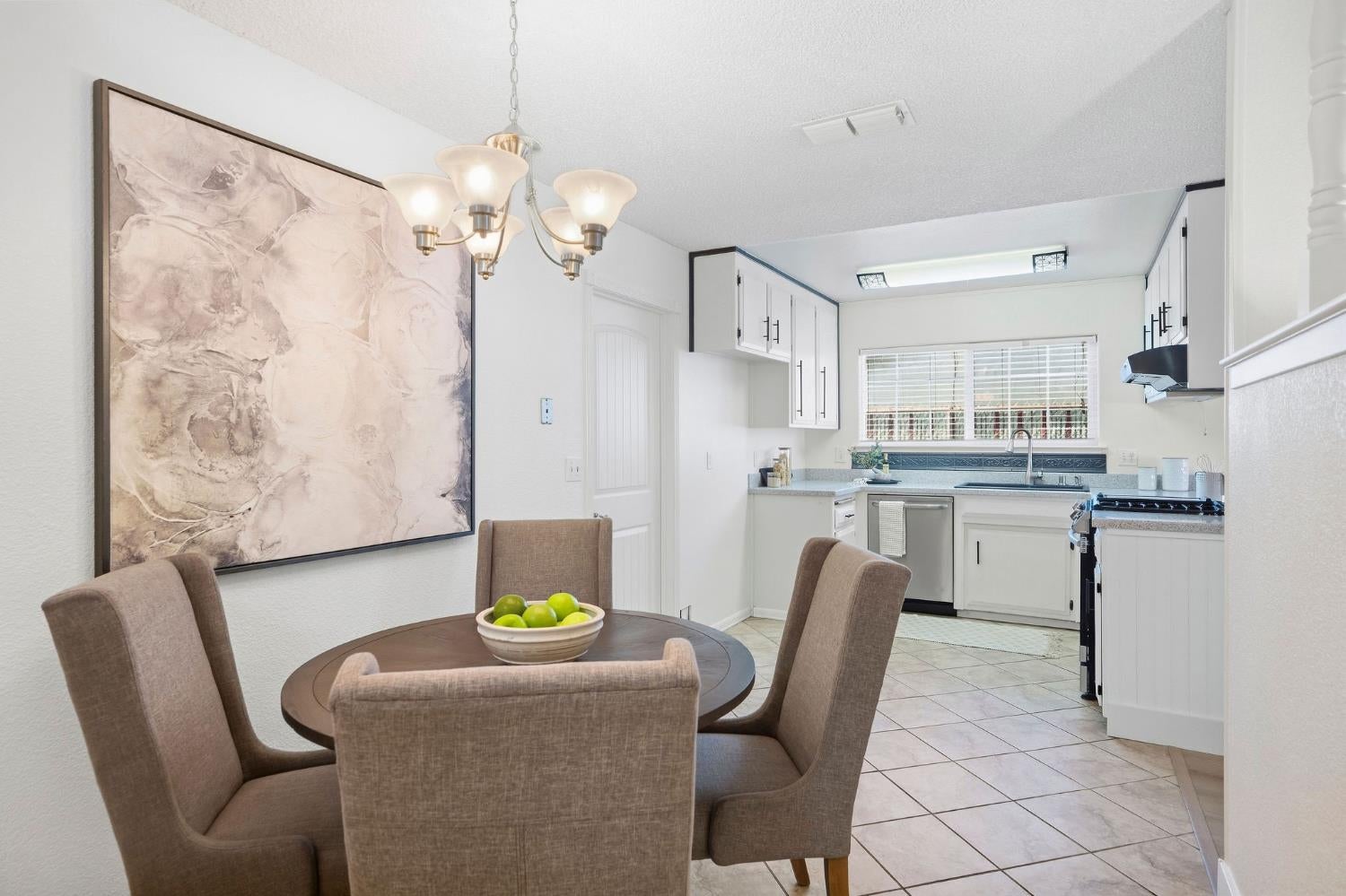 Dining area with a round table and chandelier opening into a bright kitchen with white cabinetry.