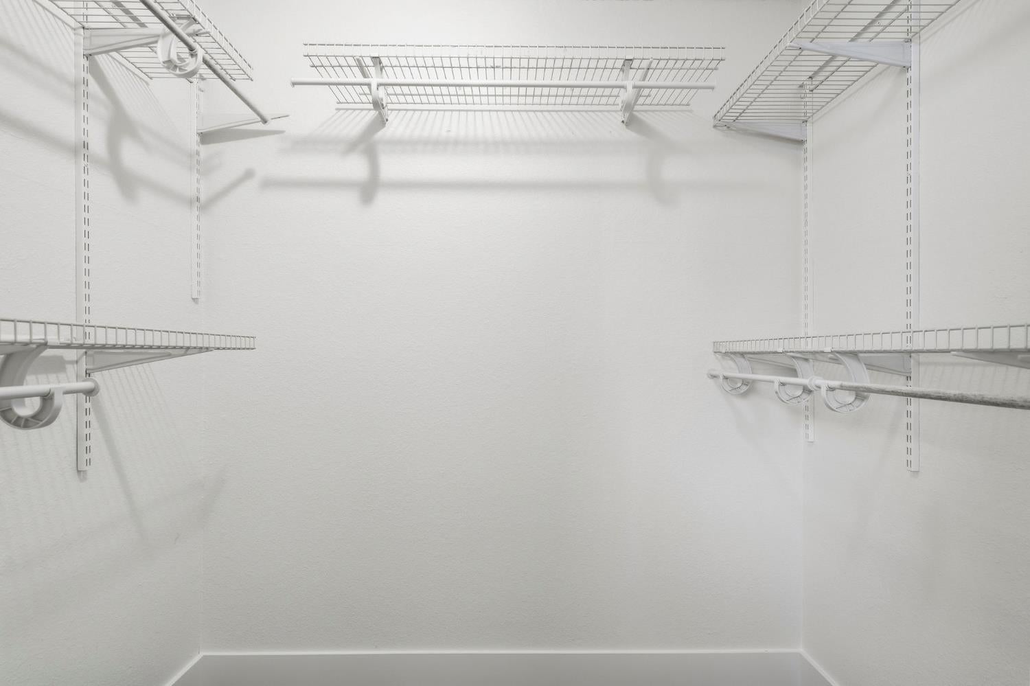 Empty walk-in closet with white wire shelving and hanging rods.