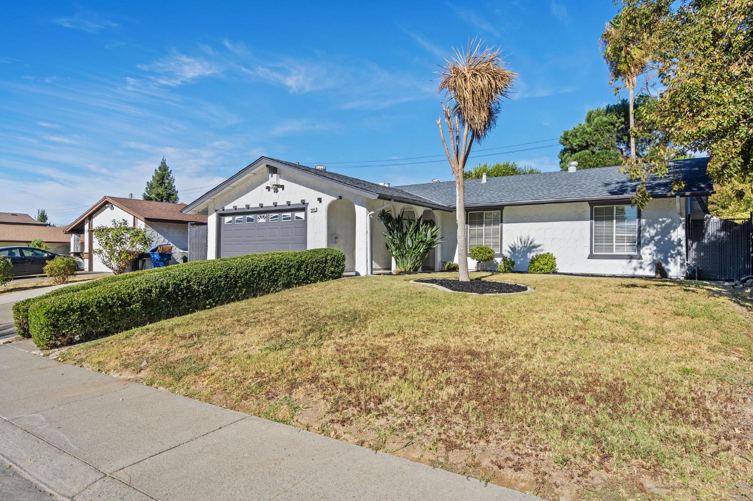 Single-story white house with an attached garage, arched entry, and trimmed front hedge.