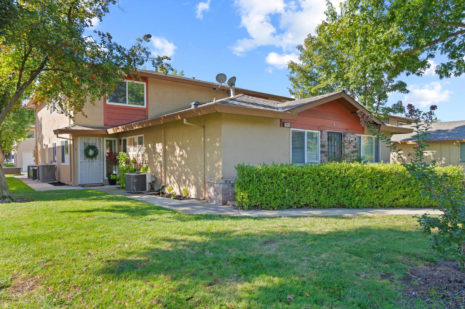 Two-story stucco residence with red gable accents, a trimmed hedge, and mature trees.