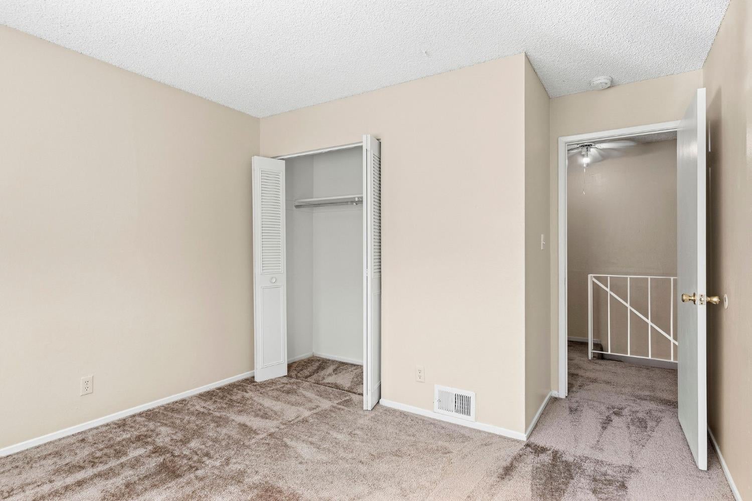 Vacant bedroom with an open louvered closet and doorway to a carpeted landing.