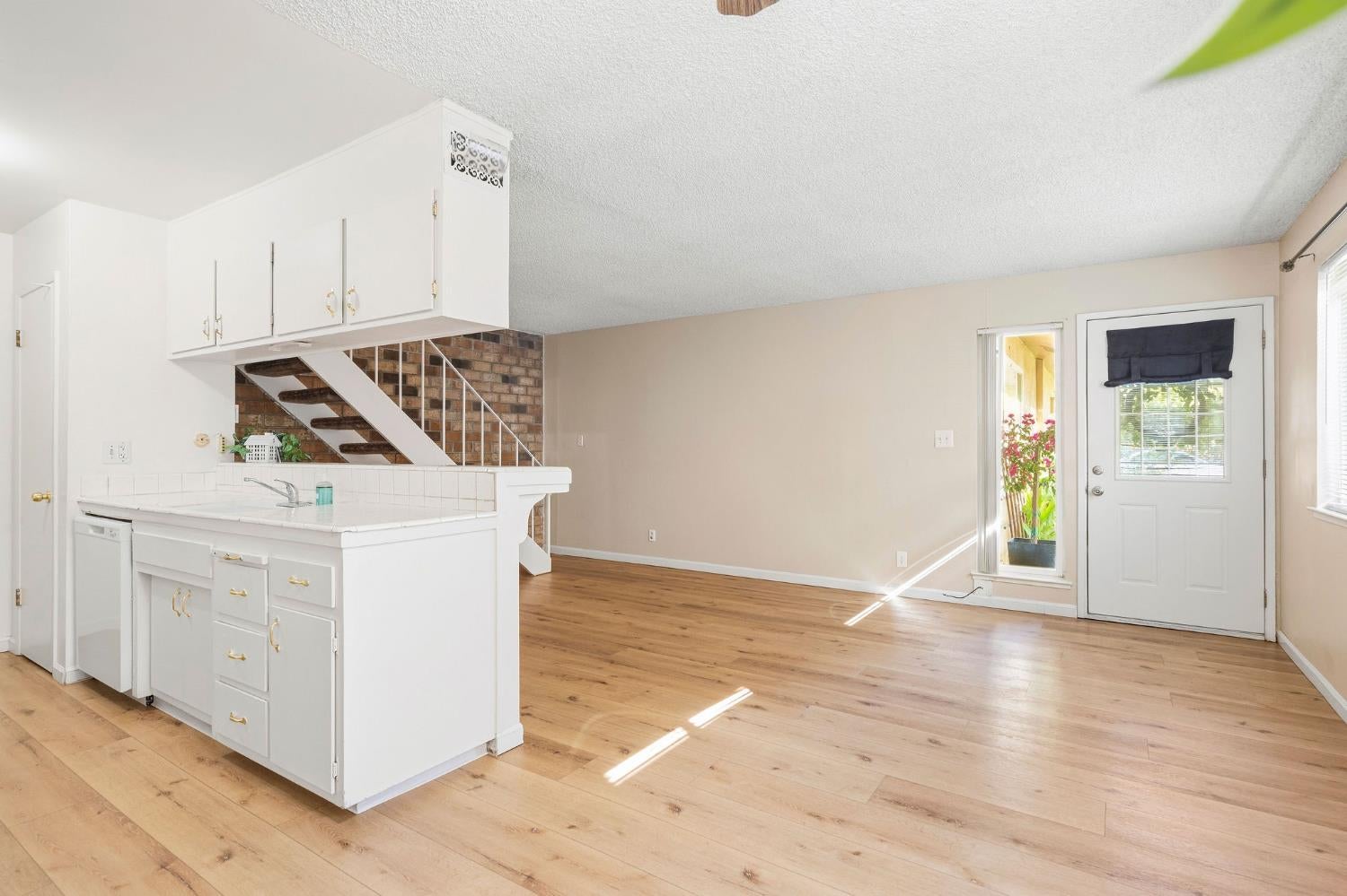 Open-plan kitchen and living area with white cabinetry, wood floors, and a brick-backed staircase.