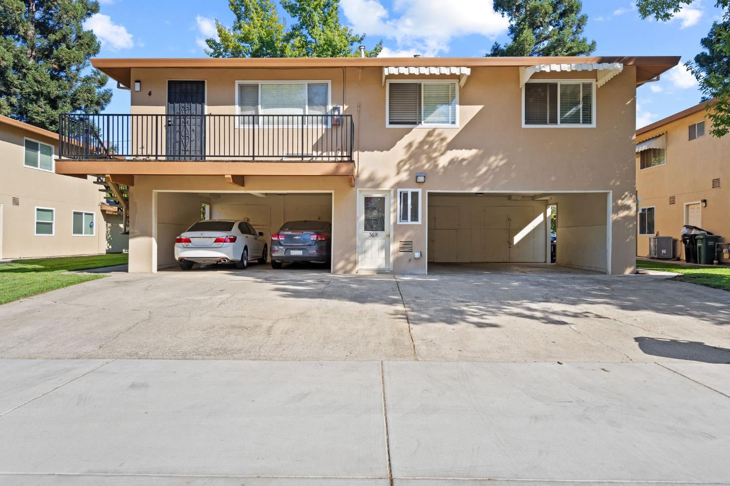 Two-story tan residential building with an upper balcony and covered parking beneath.