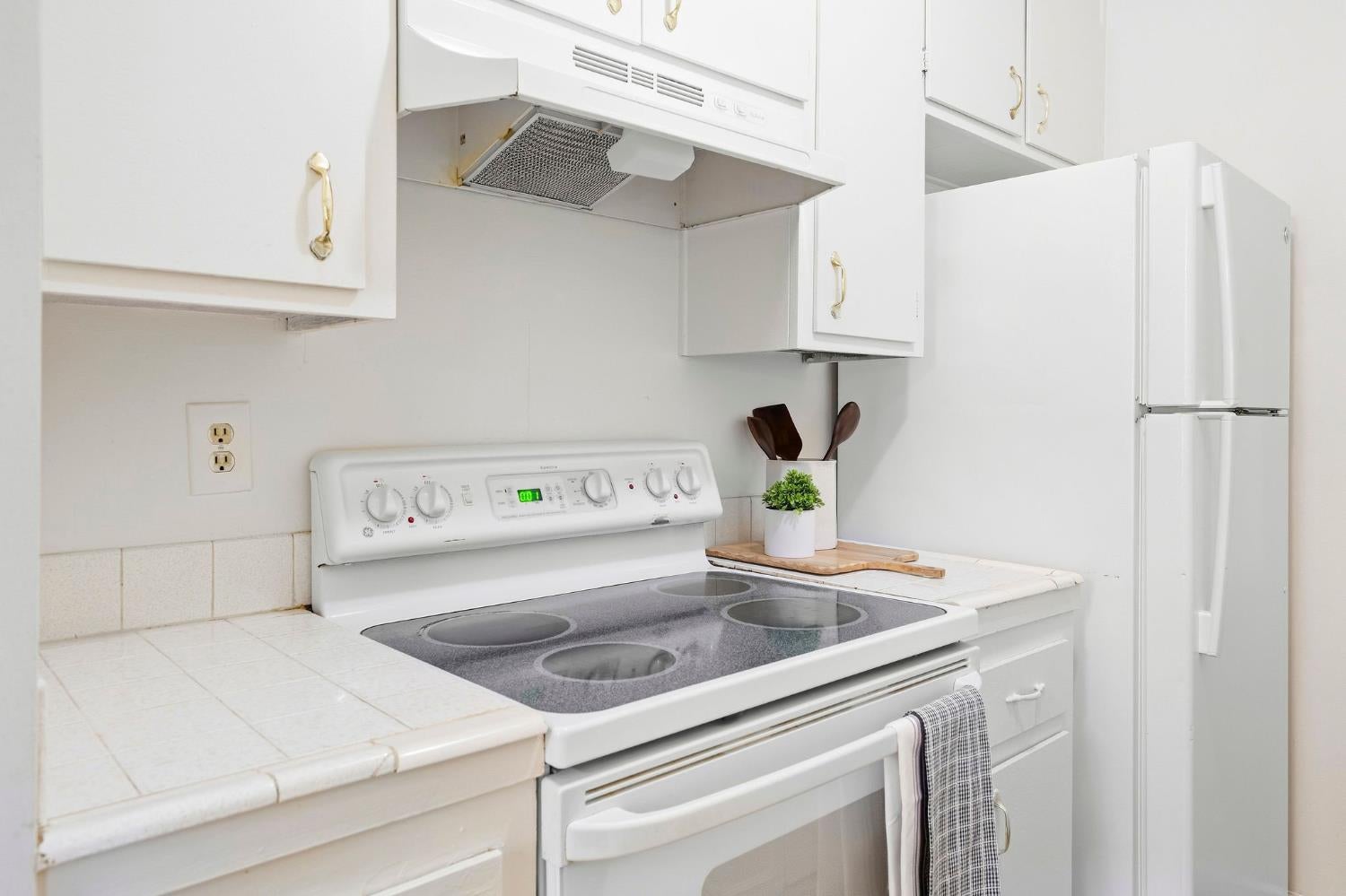 Kitchen with white cabinets, a glass-top electric range, tiled counters, and a full-size refrigerator.