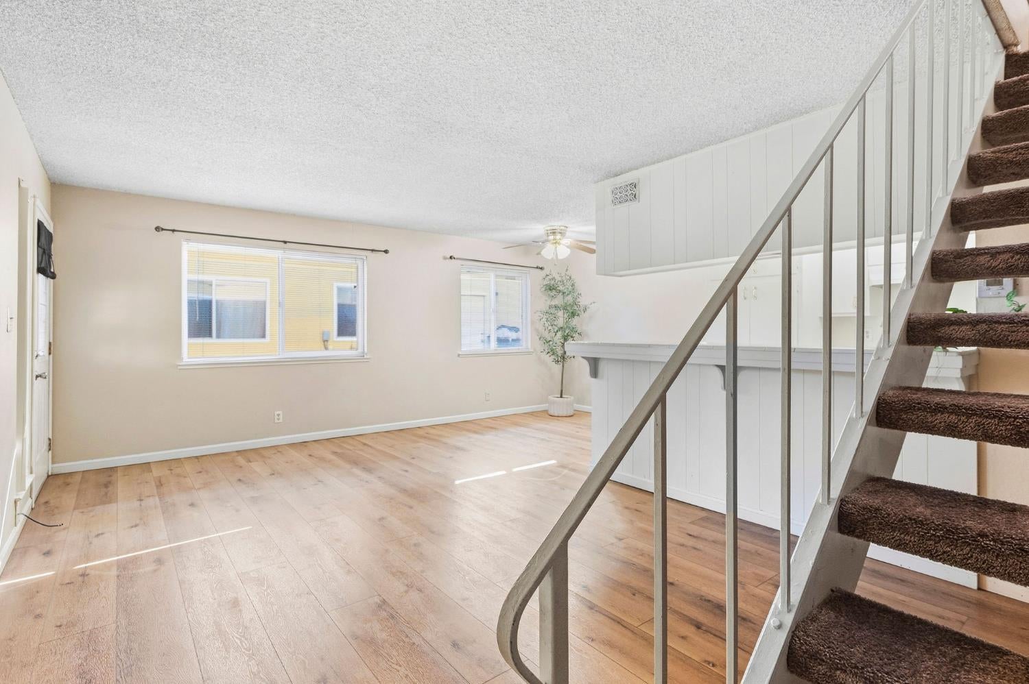 Vacant living area with light wood floors and a carpeted staircase beside the kitchen counter.